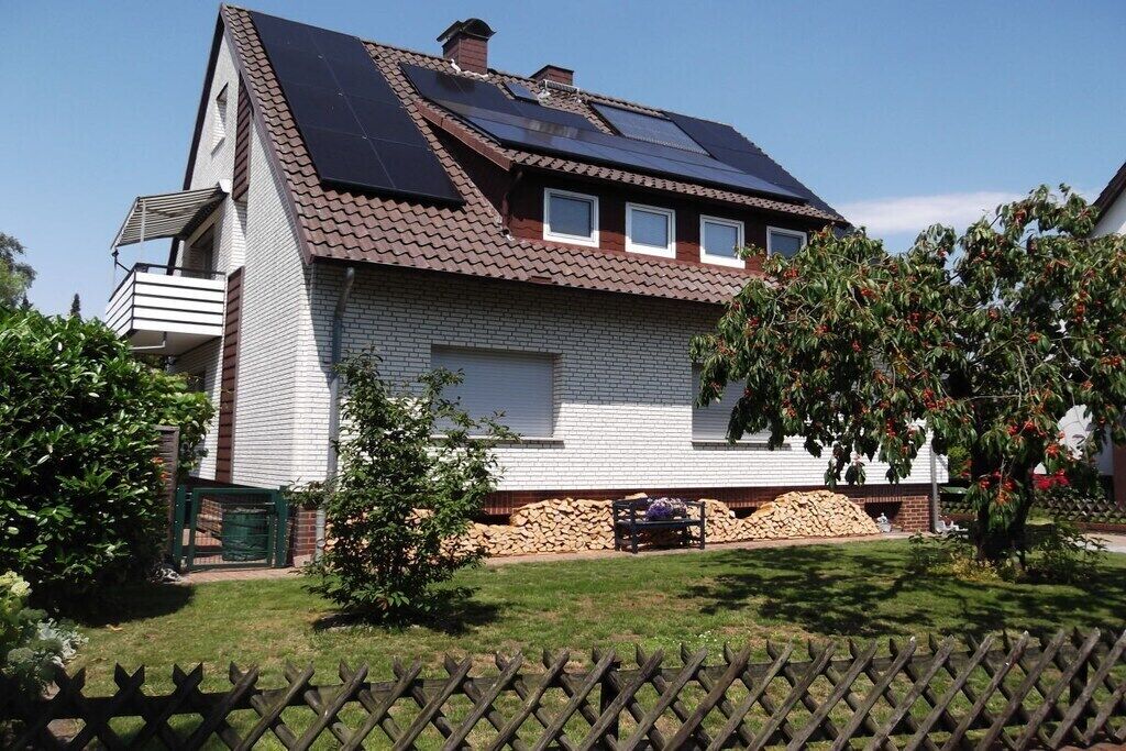 A two-story house with a sloped roof, solar panels, a brick exterior, a visible garage, and a fenced yard with a tree.