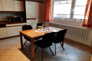 A dining area with a wooden table and black chairs, a kitchen with white cabinets and a microwave, and a window with curtains. - Holiday apartment with 2 bedrooms (Rinteln)