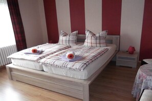 A double bed with a plaid bedspread and pillows, a bedside table with a lamp, and a window with curtains. - Holiday apartment with 2 bedrooms (Rinteln)