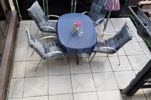 Een patio tafel met een blauwe tafelkleed, omringd door vier stoelen, en een vaas met roze bloemen.
