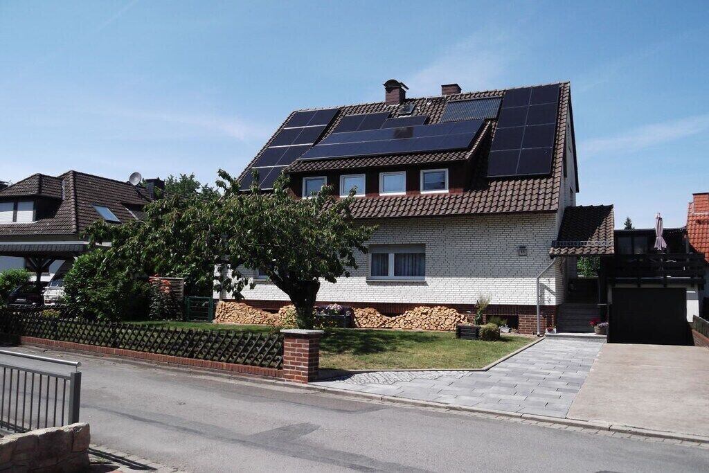 A residential building with solar panels on the roof, a brick facade, and a paved driveway.