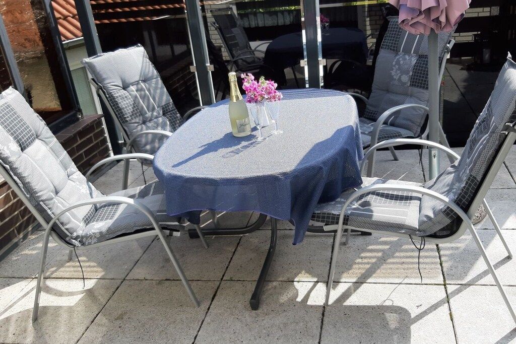 An outdoor patio with a round table covered by a blue tablecloth, surrounded by metal chairs.