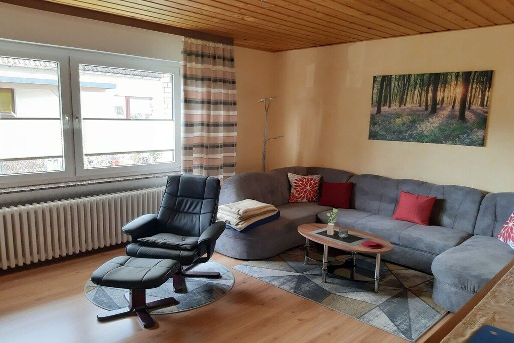Ett vardagsrum med en grå soffa, en svart kontorsstol, ett soffbord och ett element.