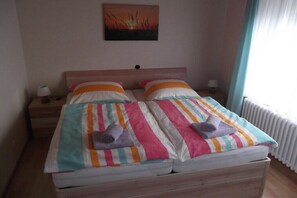 Een tweepersoonsbed met gestreepte beddengoed en twee kussens, een nachtkastje met een lamp, en een aan de muur hangend schilderij.