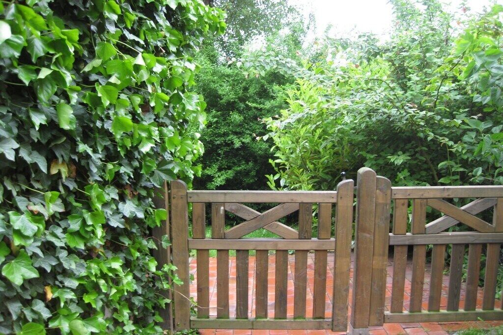 A wooden gate with a cross design, surrounded by lush green foliage.