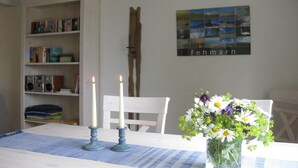 A room with a white table, two candles, a vase with flowers, a bookshelf, and a wall-mounted picture. - Holiday home in Fehmarn with swimming pool (Fehmarn)
