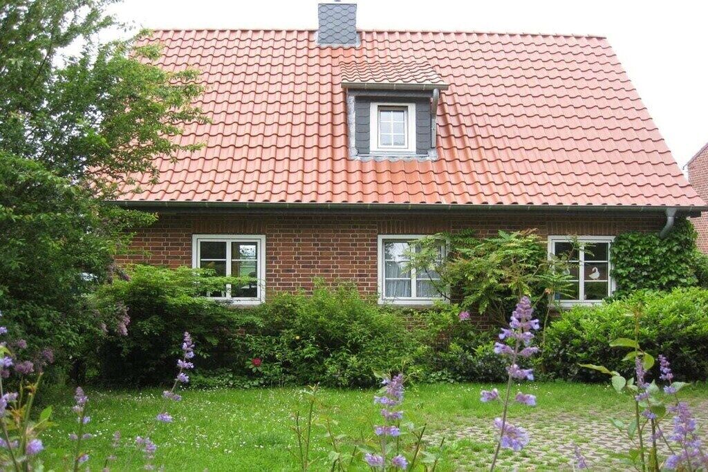 A two-story house with a red-tiled roof, brick walls, and a small window with shutters.