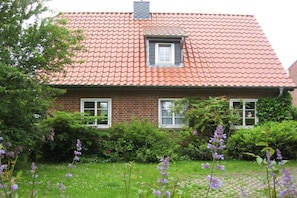 Een woonhuis met twee verdiepingen, een dak met rode tegels, bakstenen muren en een klein raam met luiken.