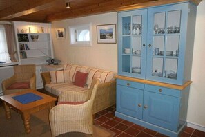 A cozy living room with wicker furniture, a blue cabinet with glass doors, and a window with a view. - Old Beach Warden's Office No. 1 (List)