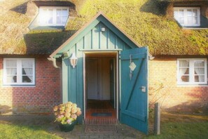 Una casa amb una porta verda, façana de maó i teulat de palla.