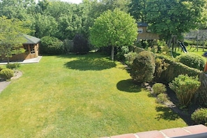 A well-maintained grassy yard with a wooden playhouse, a large tree, and a playground structure. - Holiday apartment with 1 bedroom (List auf Sylt)
