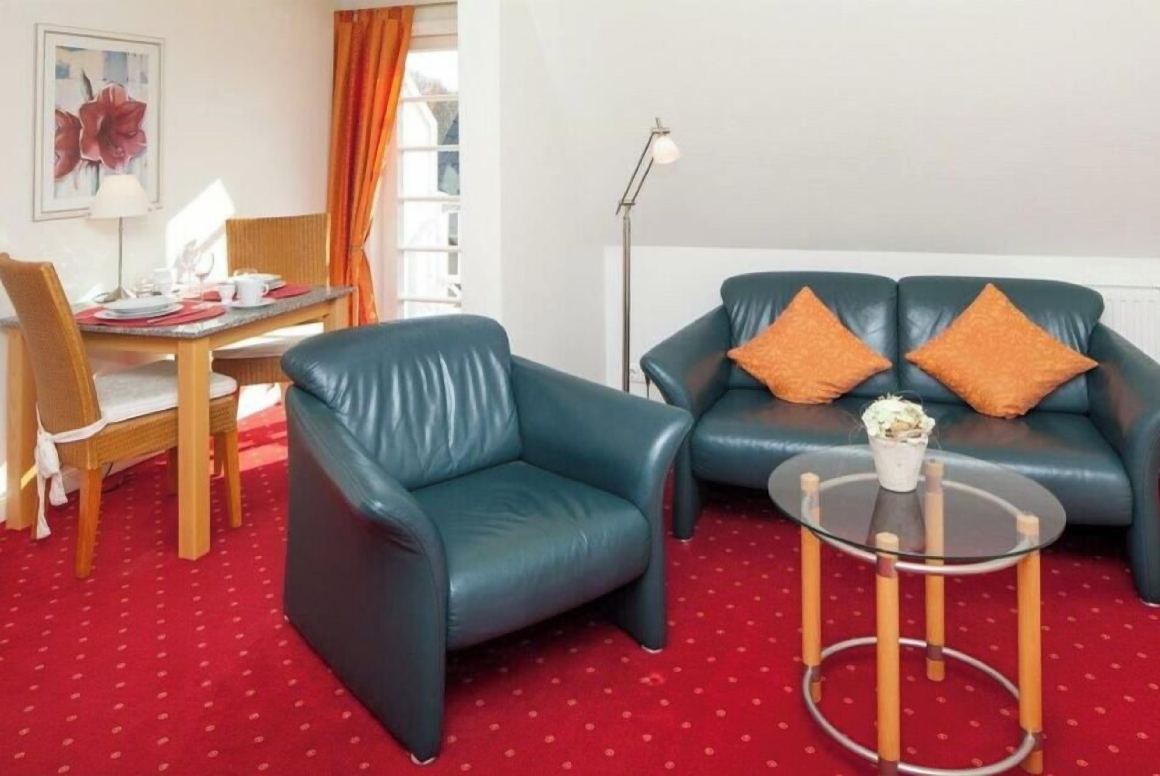 A room with a blue leather sofa, a glass coffee table, a dining table with chairs, and a floor lamp.