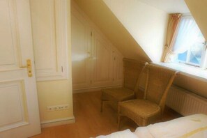 A room with a sloped ceiling, a window with curtains, a chair, and a bed. - Old Beach Warden's Office No. 2 (List auf Sylt)