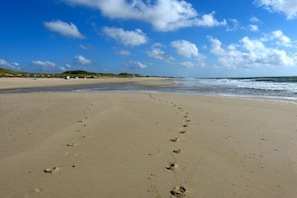 A sandy beach with footprints leading to the water, a clear sky, and distant dunes. - Old Beach Warden's Office No. 2 (List auf Sylt)