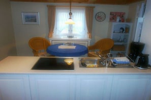 A small kitchen with a dining table, chairs, a sink, and a window with curtains. - Old Beach Warden's Office No. 2 (List auf Sylt)
