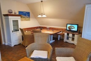 Ein Essbereich mit Korbstühlen, einem Holztisch, einem Fernseher und einer Vitrine mit Glastüren.