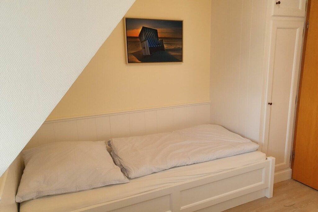 A small, single-bed room with a white headboard, a framed picture on the wall, and a wooden door.