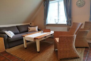 A cozy living room with a sofa, two wicker chairs, a wooden coffee table, and a window with curtains. - Country House Diedrichsen No. 3 (List auf Sylt)