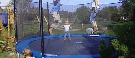 Un trampolín con red de seguridad, rodeado de césped y árboles.