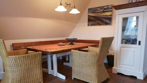 A dining area with a wooden table and wicker chairs, a hanging light fixture, and a view of the outdoors through a window. - Country House Diedrichsen No. 3 (List auf Sylt)