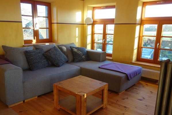 Una habitació amb un sofà gris, una taula de centre de fusta i grans finestres amb emmarcament de fusta.