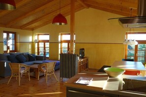 Ampla sala de estar com teto de madeira, sofá, mesa de jantar e radiador.