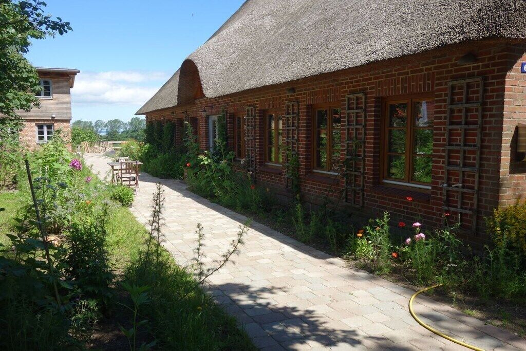 A brick building with a thatched roof, a paved walkway, and a garden with various plants and flowers.