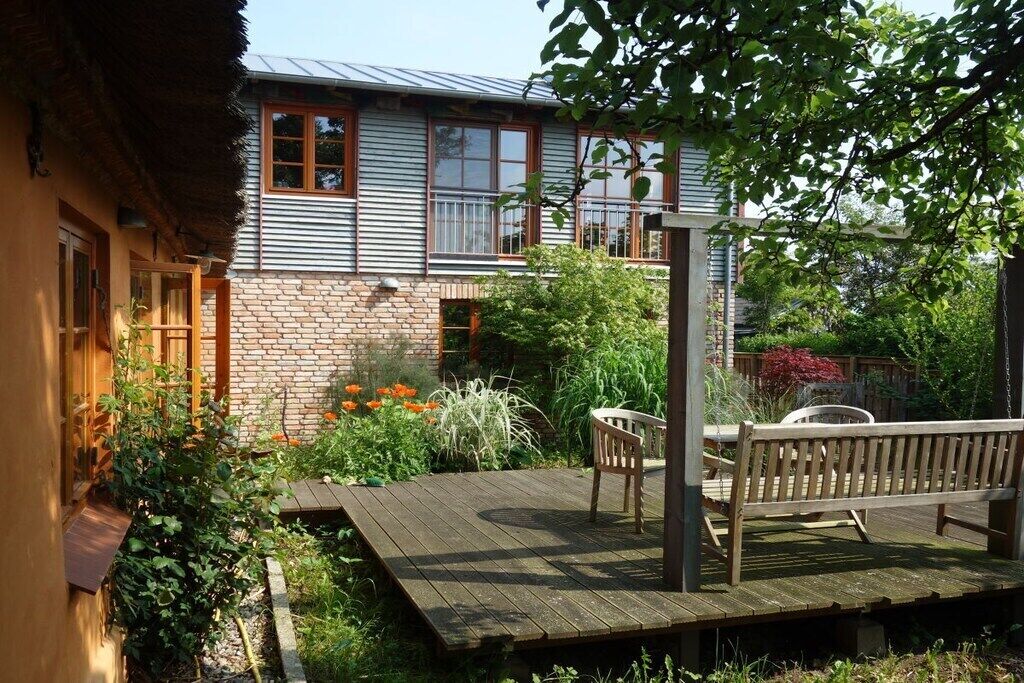 A house with a wooden deck, a bench, and a garden with various plants and flowers.