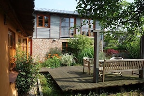 Ein Haus mit einer Holzterrasse, einer Bank und einem Garten mit verschiedenen Pflanzen und Blumen.