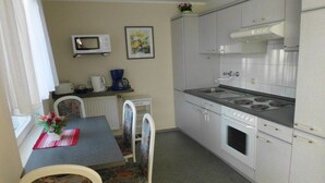 A compact kitchen with a microwave, stove, and a dining area with a table and chairs. - in Putbus - Kummer family (Putbus)