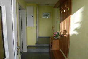 Un couloir avec une porte en bois, un petit escalier et un tableau accroché au mur.