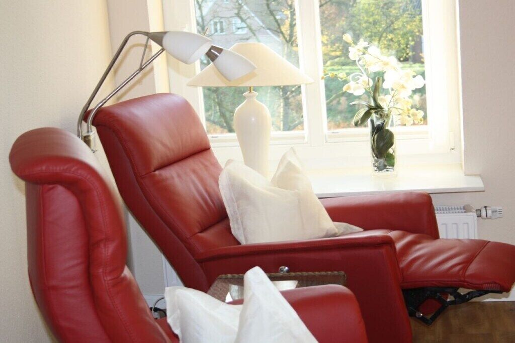 Un sillón rojo de cuero con un cojín blanco, una lámpara de pie y un florero con flores en un alféizar.