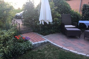 A patio area with a wicker chair, a table with a blue tablecloth, and a white umbrella. - 1 Hein Garrn Fruit Farm (mittelnkirchen)