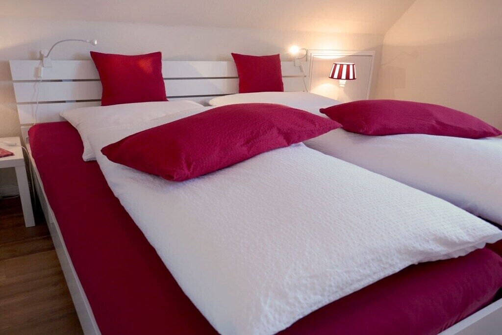 A bed with white and red bedding, a white headboard, and a bedside lamp.