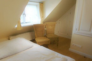 A bedroom with a bed, two wicker chairs, a window with curtains, and a radiator. - Old Beach Warden's Office 3 (List auf Sylt)