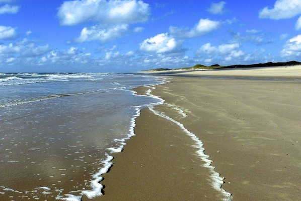 Een strand met golven die de kust bereiken, een heldere lucht en heuvels in de verte.