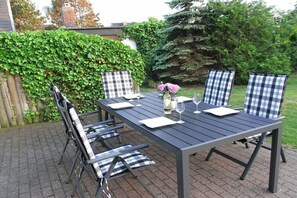 Een terras buiten met een rechthoekige tafel en vier stoelen, elk met een geruit kussen.