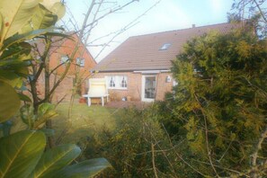 Ett bostadshus med en fasad av tegel, ett tak täckt med takpannor och en framträdgård med täta buskage.
