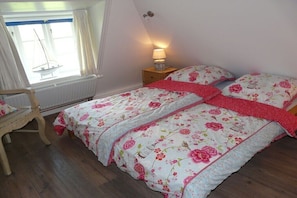Ein Schlafzimmer mit einem Bett, einem Nachttisch, einem Sessel und einem Fenster mit Vorhängen.