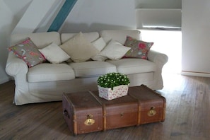 A beige sofa with floral cushions, a small potted plant, and two wooden chests with locks. - Witthuis - Pearl on the dike (Emmelsbüll - Horsbüll)