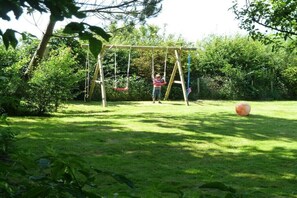 A wooden swing set in a grassy area with dense foliage in the background. - Witthuis - Pearl on the dike (Emmelsbüll - Horsbüll)