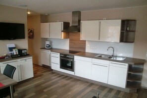 Eine moderne Küche mit weißen Schränken, einem Einbauofen, einer Kaffeemaschine und einem an der Wand montierten Flachbildfernseher.