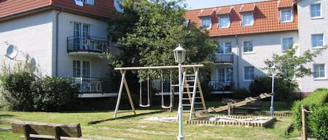 Un edificio residenziale con tetto in tegole rosse, altalene e una panchina di legno nel giardino.
