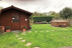A wooden cabin with a door, a hot tub, and a well-maintained lawn with stepping stones. - Holiday home in List with sauna and Wi-Fi (List)