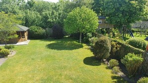 A well-maintained grassy yard with a wooden playhouse, a large tree, and a playground structure. - Holiday apartment in List with swimming pool (List)