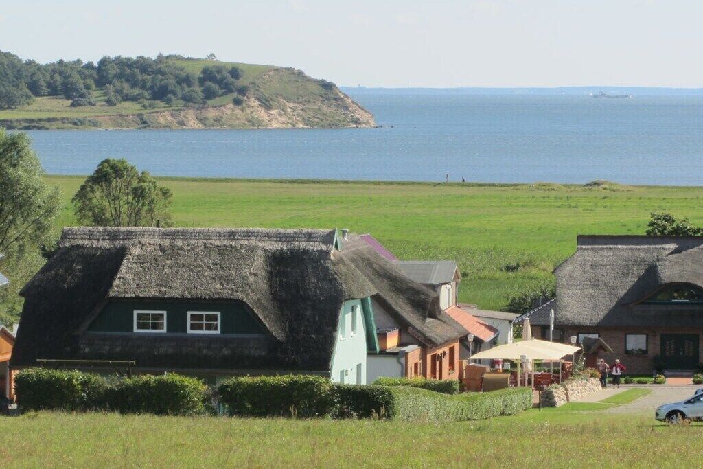 Un pueblo costero con casas tradicionales de techo de paja, un campo cubierto de hierba y una masa de agua al fondo.