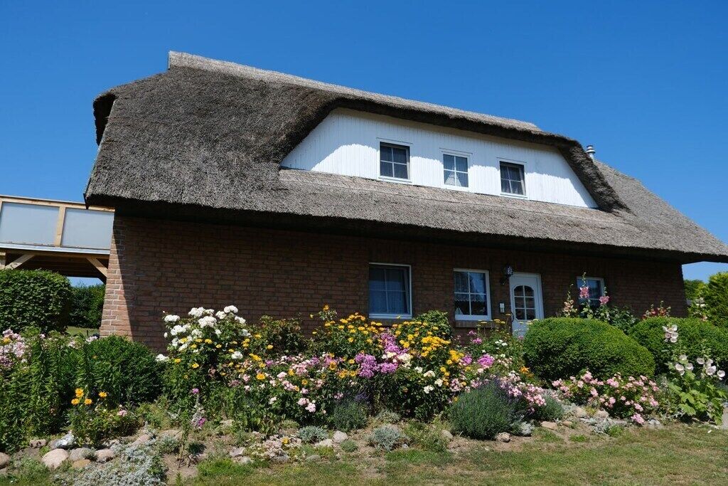 A traditional house with a thatched roof, a brick lower section, and a front garden with various flowers.