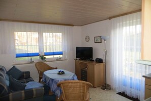 Ein Zimmer mit einer Couch, einem Tisch, einem Fernseher und einer Lampe.
