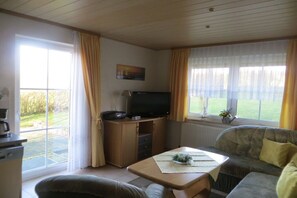 Ein Wohnzimmer mit einer Couch, einem Couchtisch, einem Fernseher auf einer Kommode und einem Fenster mit Vorhängen.