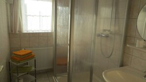 Un bany amb dutxa trencaglaçant, un lavabo i una barra de tovalloles amb tovalloles doblegades.